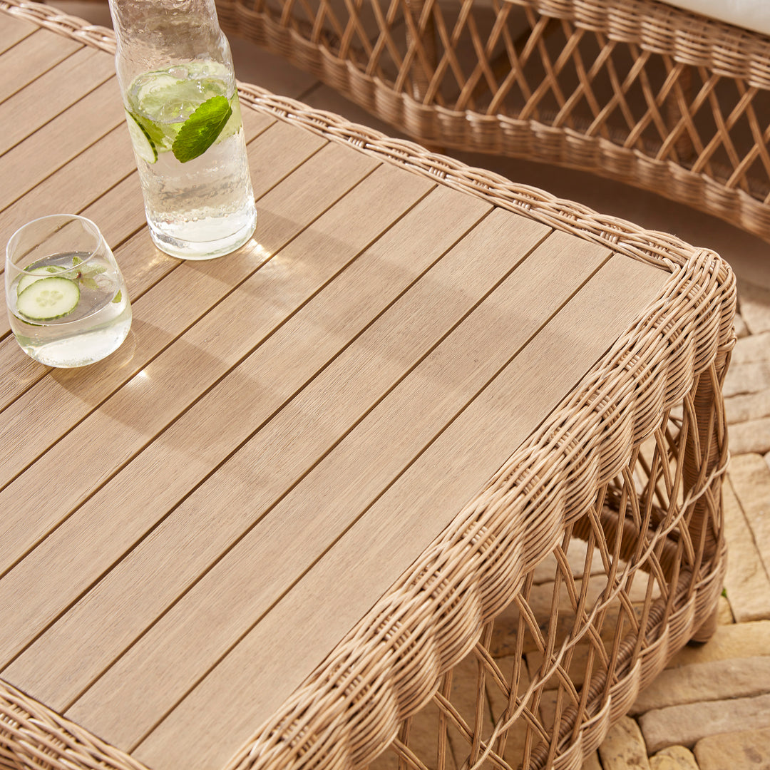 Close-up of an elegant wicker coffee table with a natural acacia wood top, featuring glass of cucumber water, perfectly styled for relaxed outdoor lounging