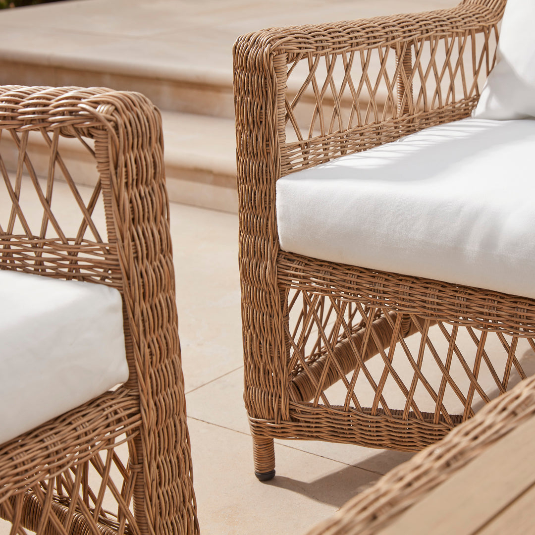 Close-up of an elegant wicker armchairs with deep comfortable white seat and back cushions.