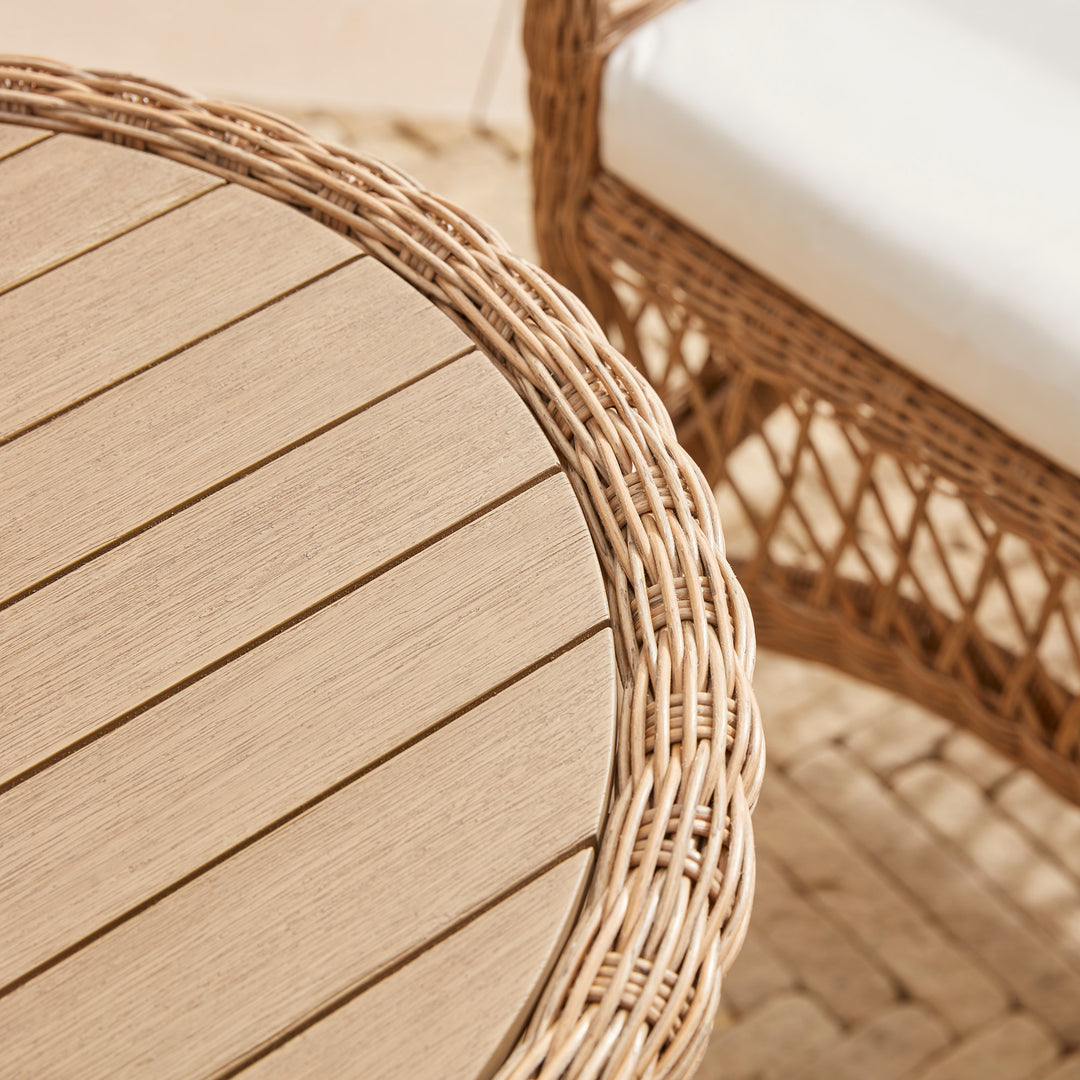 Close up detail of round wooden garden table set within a wicker rattan frame, alongside a matching wicker garden chair