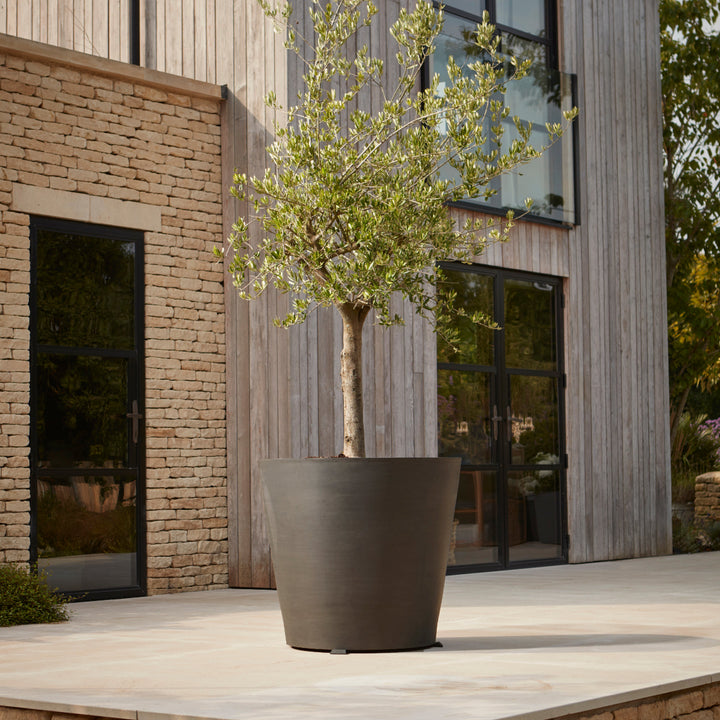 Tall contemporary black planter with a sleek matte finish, styled with a tree on a modern patio for a minimalist outdoor aesthetic.