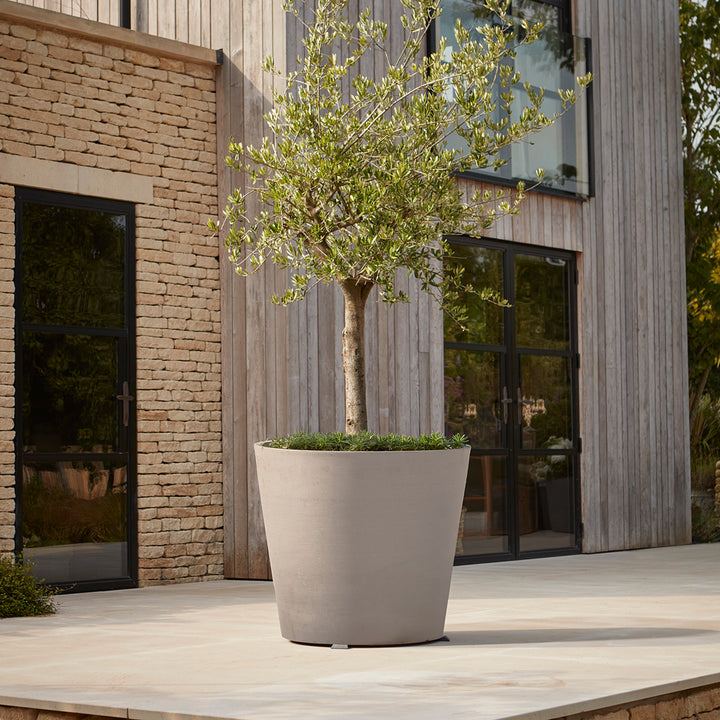 Tall contemporary taupe planter with a sleek matte finish, styled with a tree on a modern patio for a minimalist outdoor aesthetic.