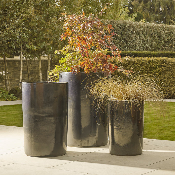 Set of tall black glazed plant pots in varying heights, styled on a garden patio with ornamental grasses and Japanese maple.