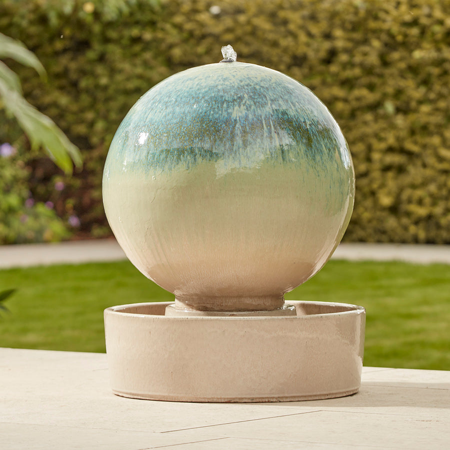 Extra-large globe-shaped ceramic water feature with a soft blue-green glaze and integrated basin, styled on a garden patio.