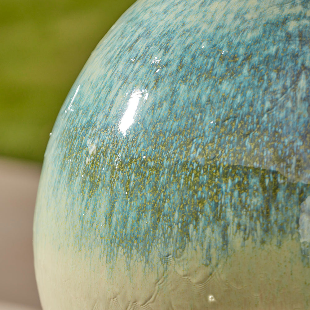 Water bubbling from the top of a large glazed globe fountain with glossy ceramic finish and flowing water detail.