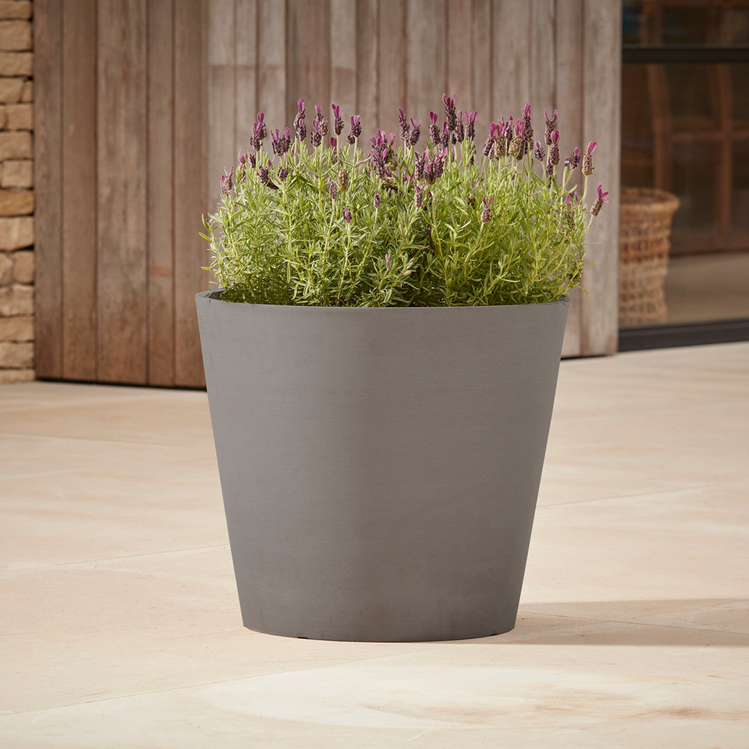 Gardenesque x EcoPots Round Plant Pot in grey featuring a sleek conical shape, placed on a patio with lavender plants.