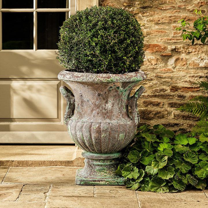 Large urn planter in turquoise aged glaze with ribbed body and handles, displayed with boxwood topiary outdoors.