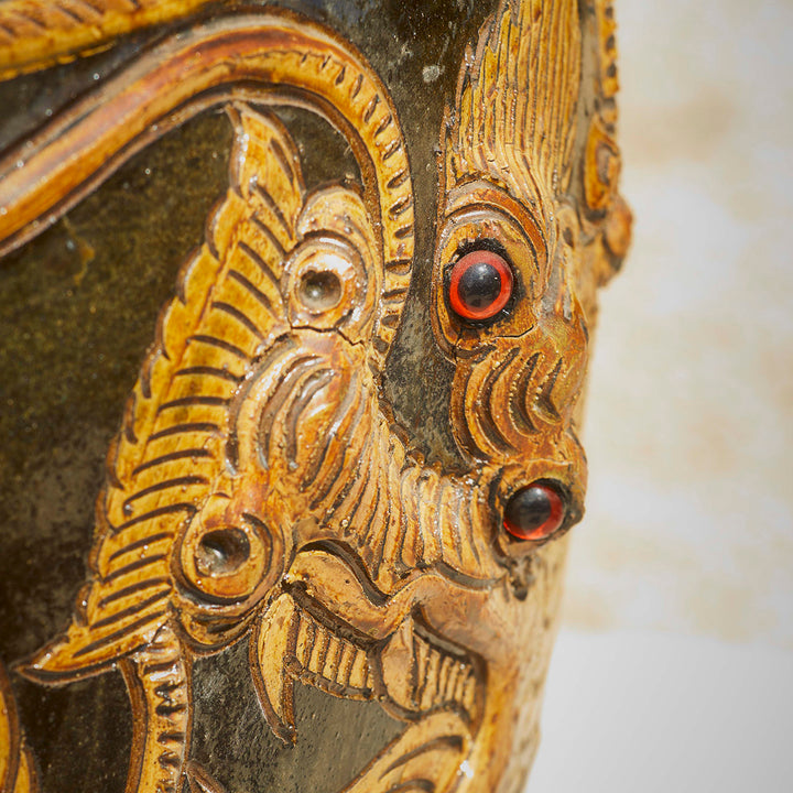 Close-up of ornate dragon face on a handcrafted Chinese ceramic pot, showcasing textured detailing and red glass-like eyes.