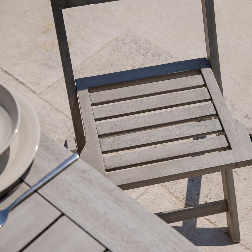 Detail of slatted wooden dining chair from the Repton garden set in light grey finish on a stone terrace.