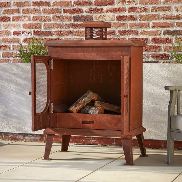 A Rustic garden wood burner set on a cotswold patio. The mesh doors are open and the the logs are stacked inside ready to be light.