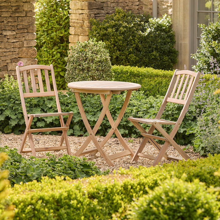 Wooden outdoor table and chairs in a garden setting with greenery.