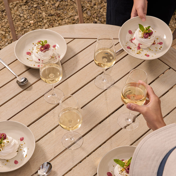 People enjoying a meal with white wine on a wooden table outdoors.