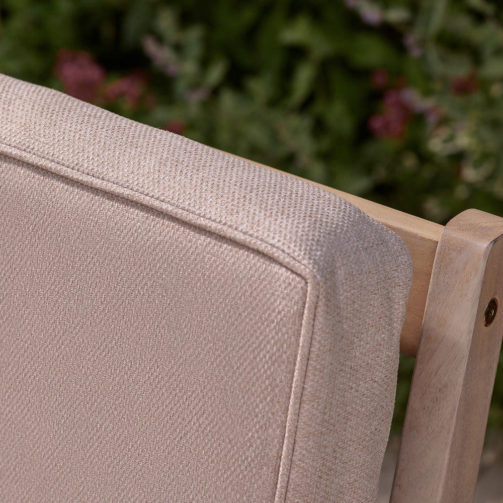 Close-up of oatmeal cushion backrest on wooden outdoor armchair, showing textured fabric and piped edge.