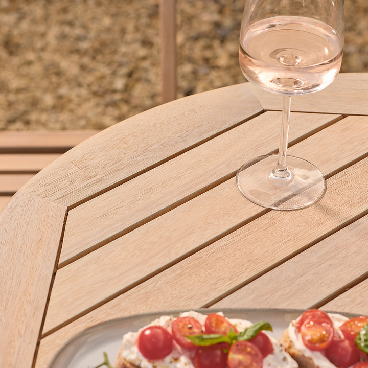 Wine glass with a light pink beverage on a wooden table outdoors.