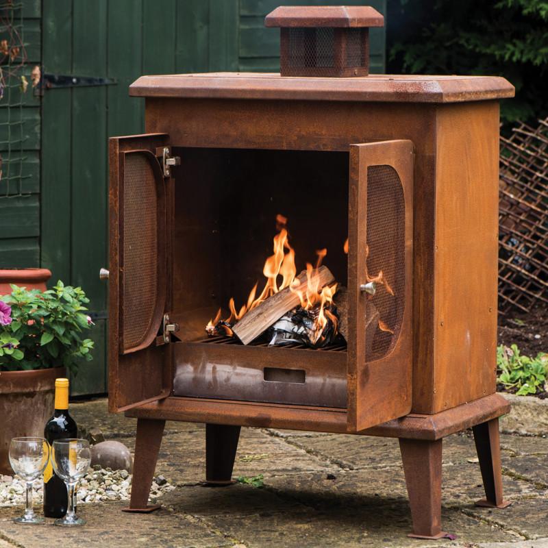 Wakehurst Outdoor Wood Burning Fireplace with its mesh doors open, displaying a strong burning fire. A durable steel garden heater with a rusted finish for a vintage aesthetic.