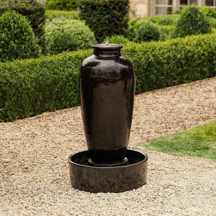 Tall black urn water feature with high gloss glaze, creating a striking garden focal point.
