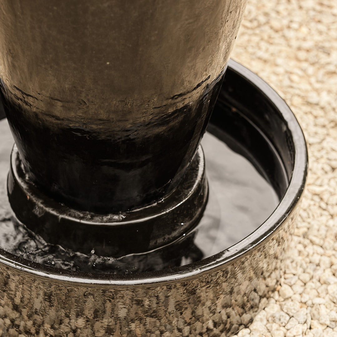 Close-up of black urn water feature base with circular reservoir collecting water.