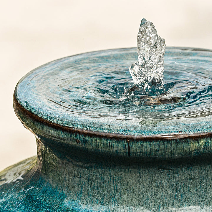 Close-up of water bubbling from top of blue urn water feature, finished in a reactive glaze.