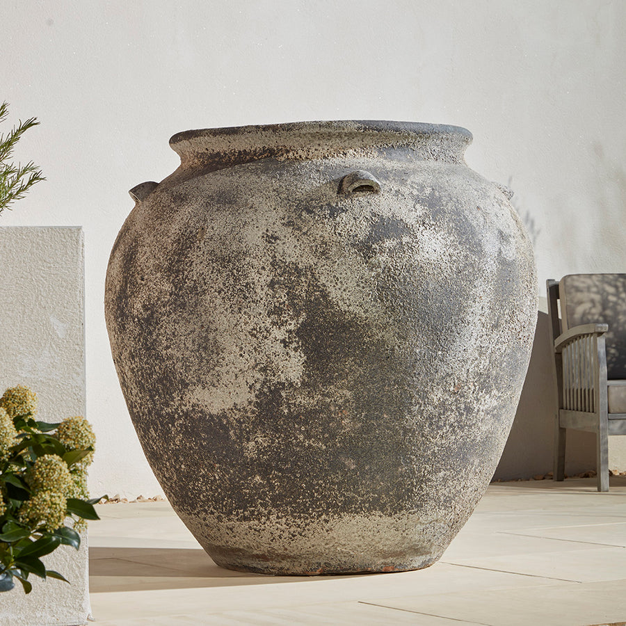 Extra Large 110cm wide stone antique effect jar  for plants on a Mediterranean patio. Next to a wooden garden chair to show how large the pot is 
