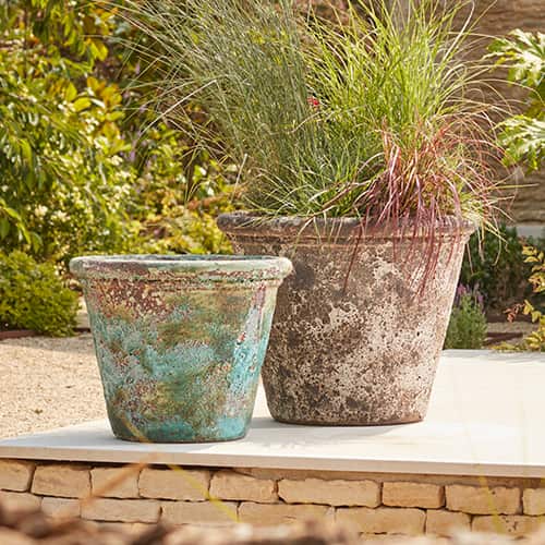 two ancient stone garden plant pots on a patio, planted with structural grasses 