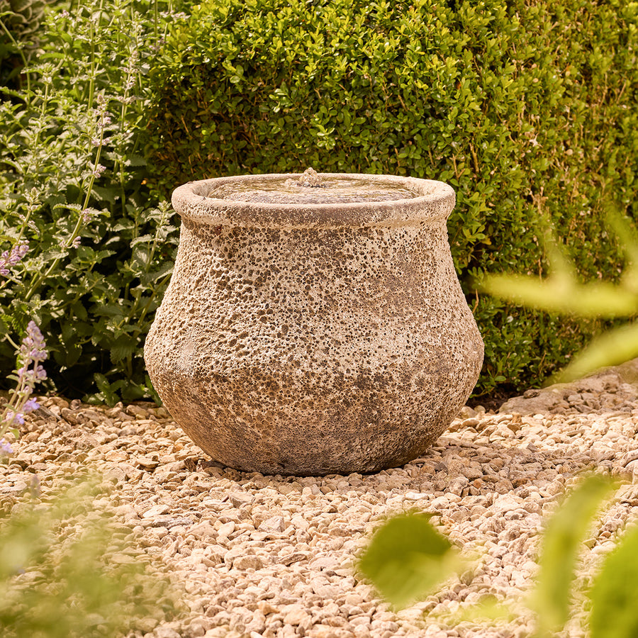 Decorative stone water feature on a gravel surface with greenery in the background