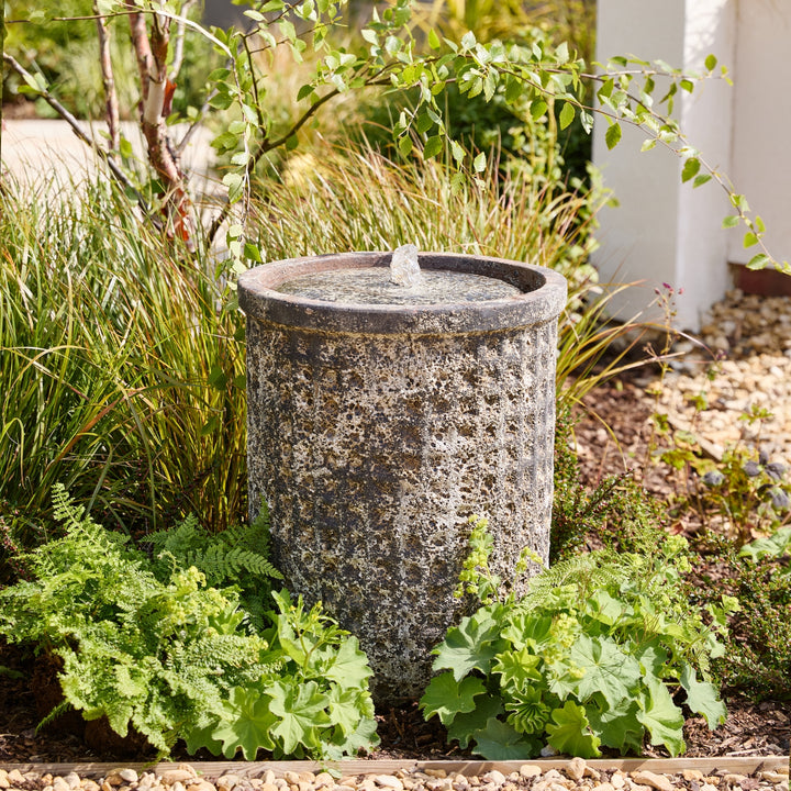 Decorative stone water feature in a garden setting with plants and gravel.