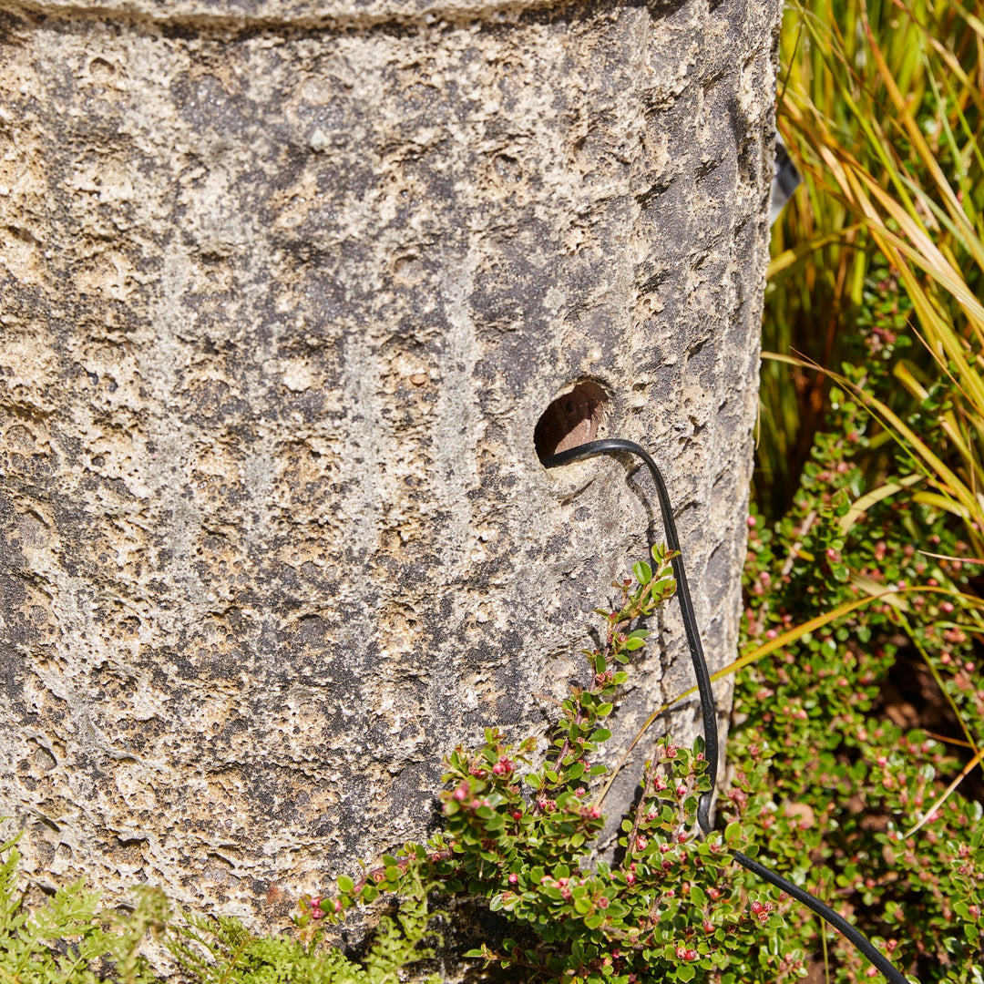 Cable running along a stone wall with greenery in the background