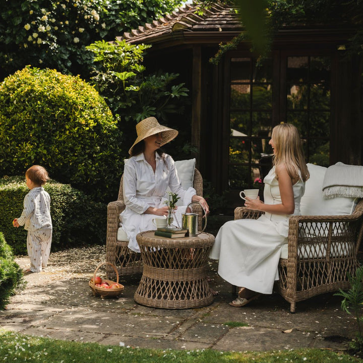 Two women and a child sitting outdoors in a garden setting, enjoying tea on luxurious deep garden armchairs