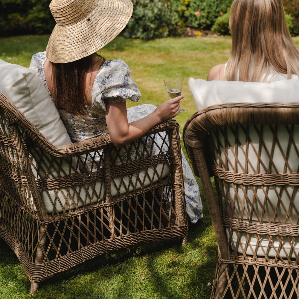 Two women sitting in wicker chairs outdoors, one holding a glass of wine.
