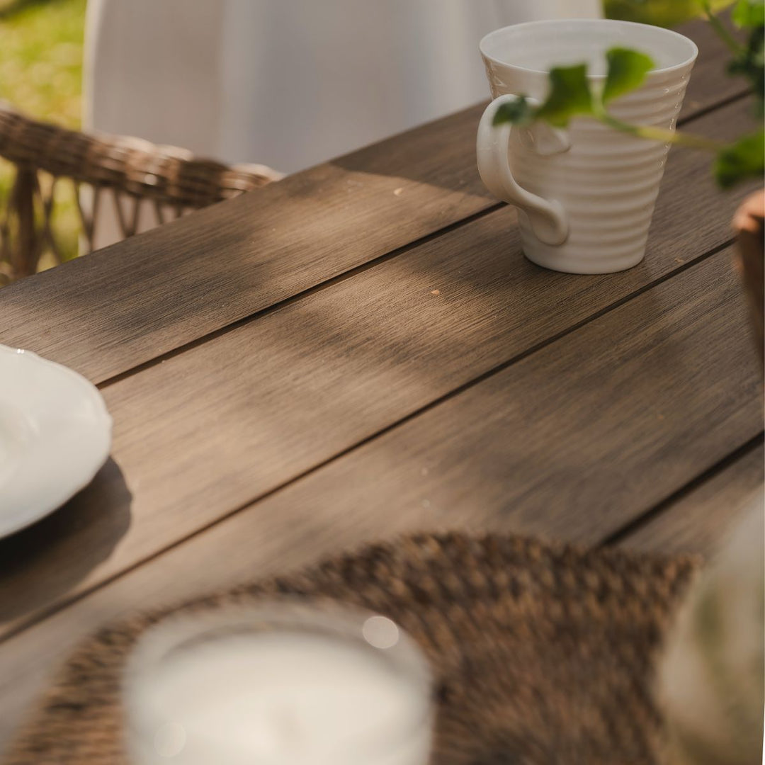 White ceramic cup on a wooden garden table with a blurred background. The wood has a beautiful natural grain 