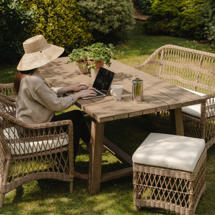 Person using a laptop at an outdoor wooden table with garden furniture.