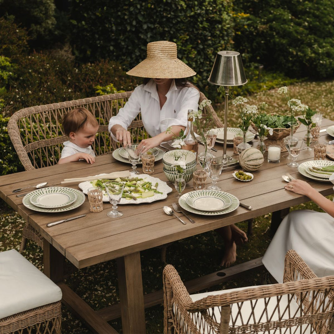 Woman and child sitting at a wooden outdoor table with a meal, surrounded by garden greenery.