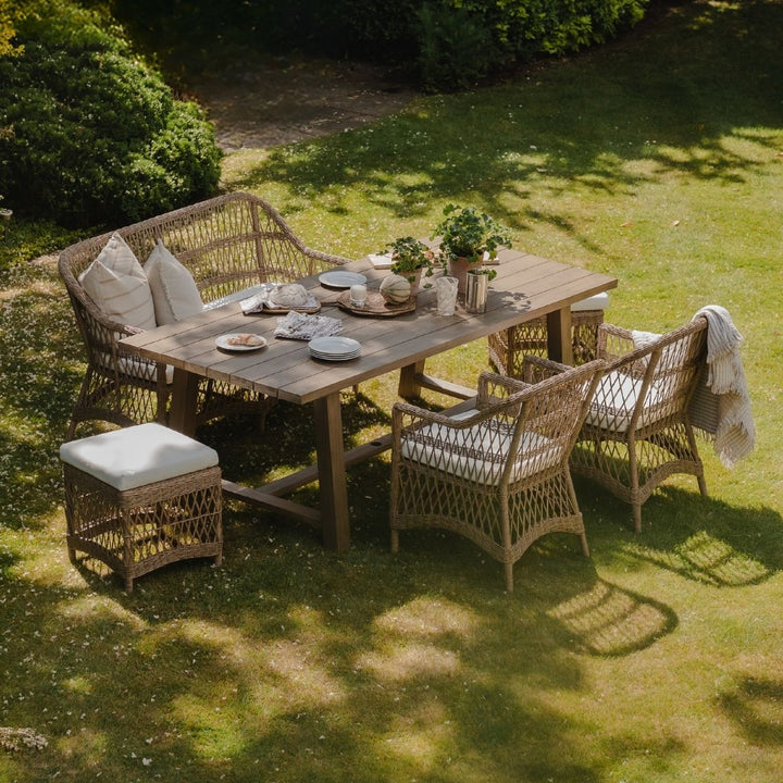 Outdoor dining setup with all-weather wicker furniture on a grassy lawn. Sturdy wooden farmhouse table set for a casual lunch in the garden.