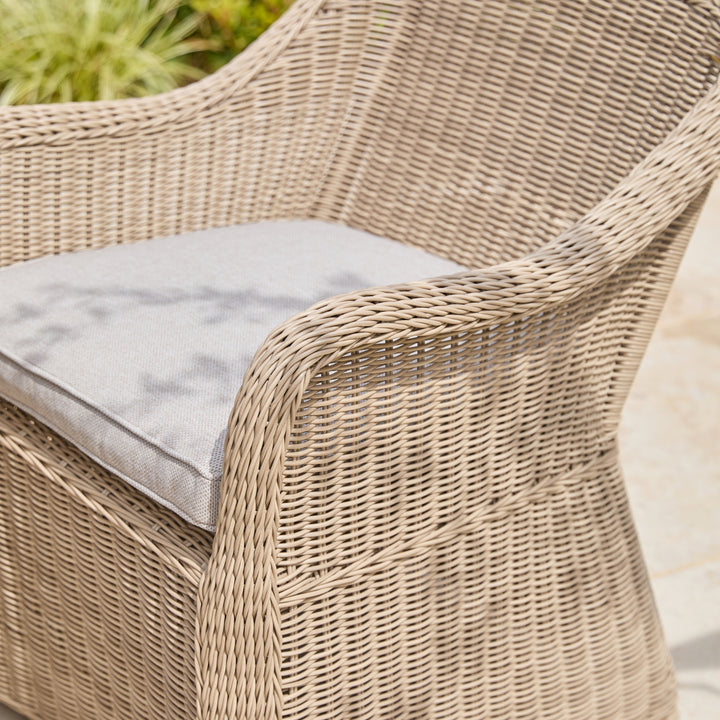 Close-up of a woven outdoor chair with a light gray cushion, showing the textured wicker material and part of the seat and backrest.