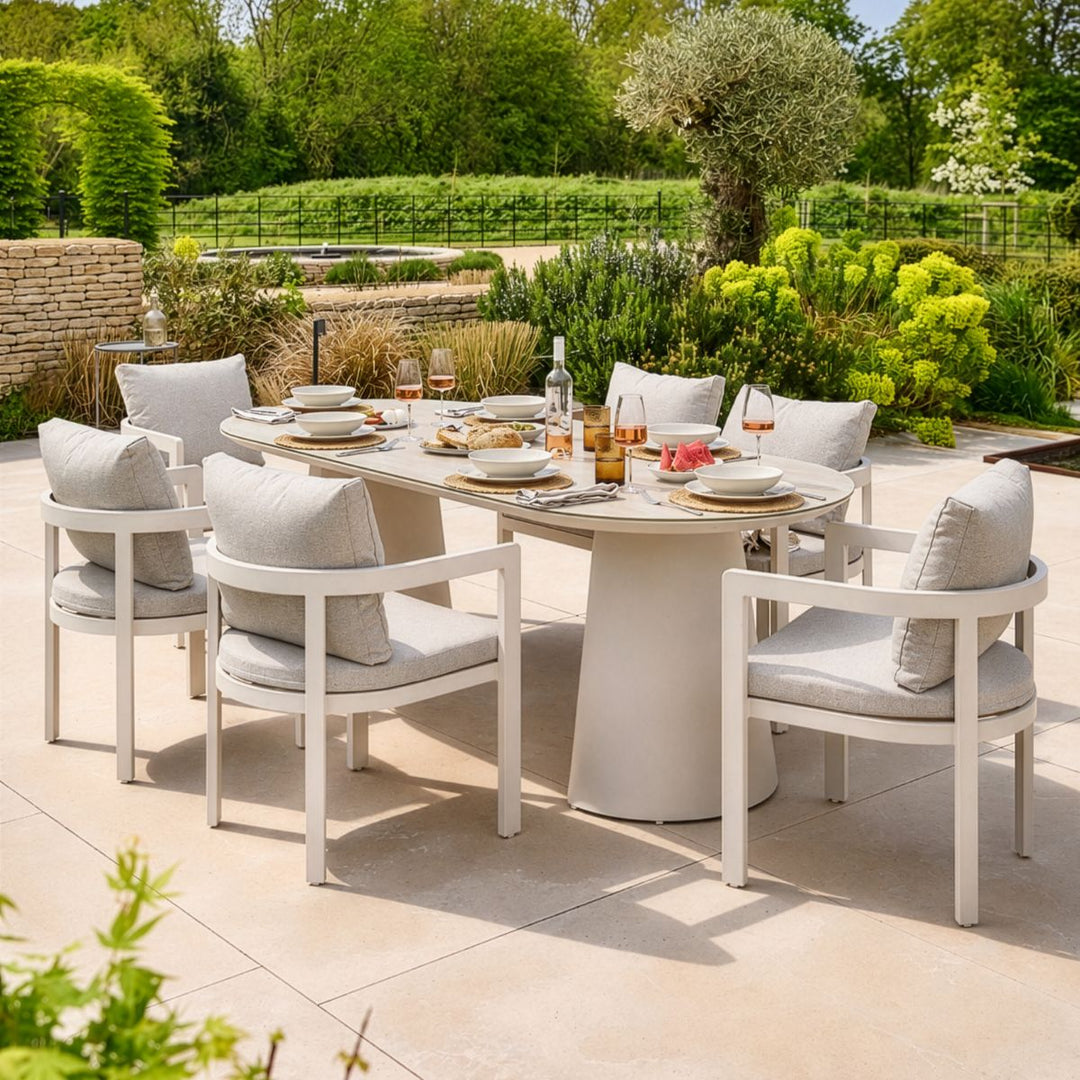Outdoor dining setup with a round table and chairs on a patio, surrounded by greenery.