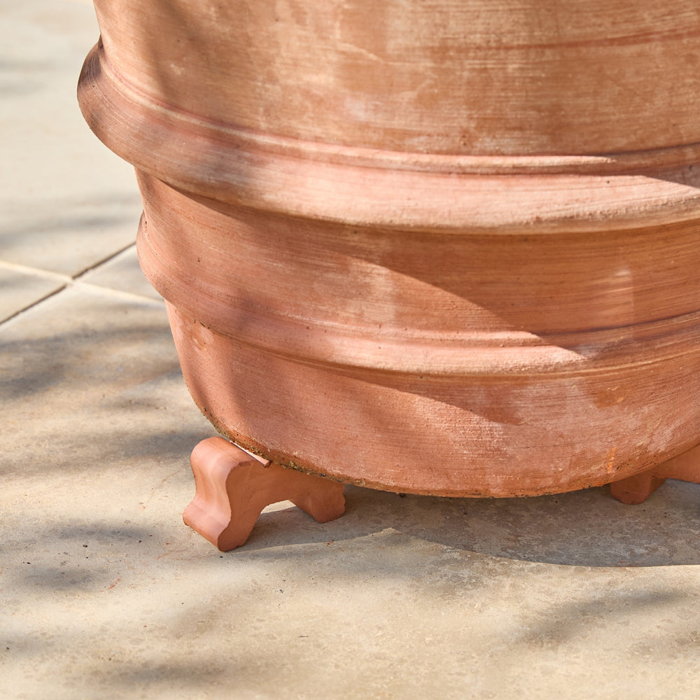 Close-up of a terracotta planter pot with a rustic, weathered finish, resting on a light concrete patio surface.