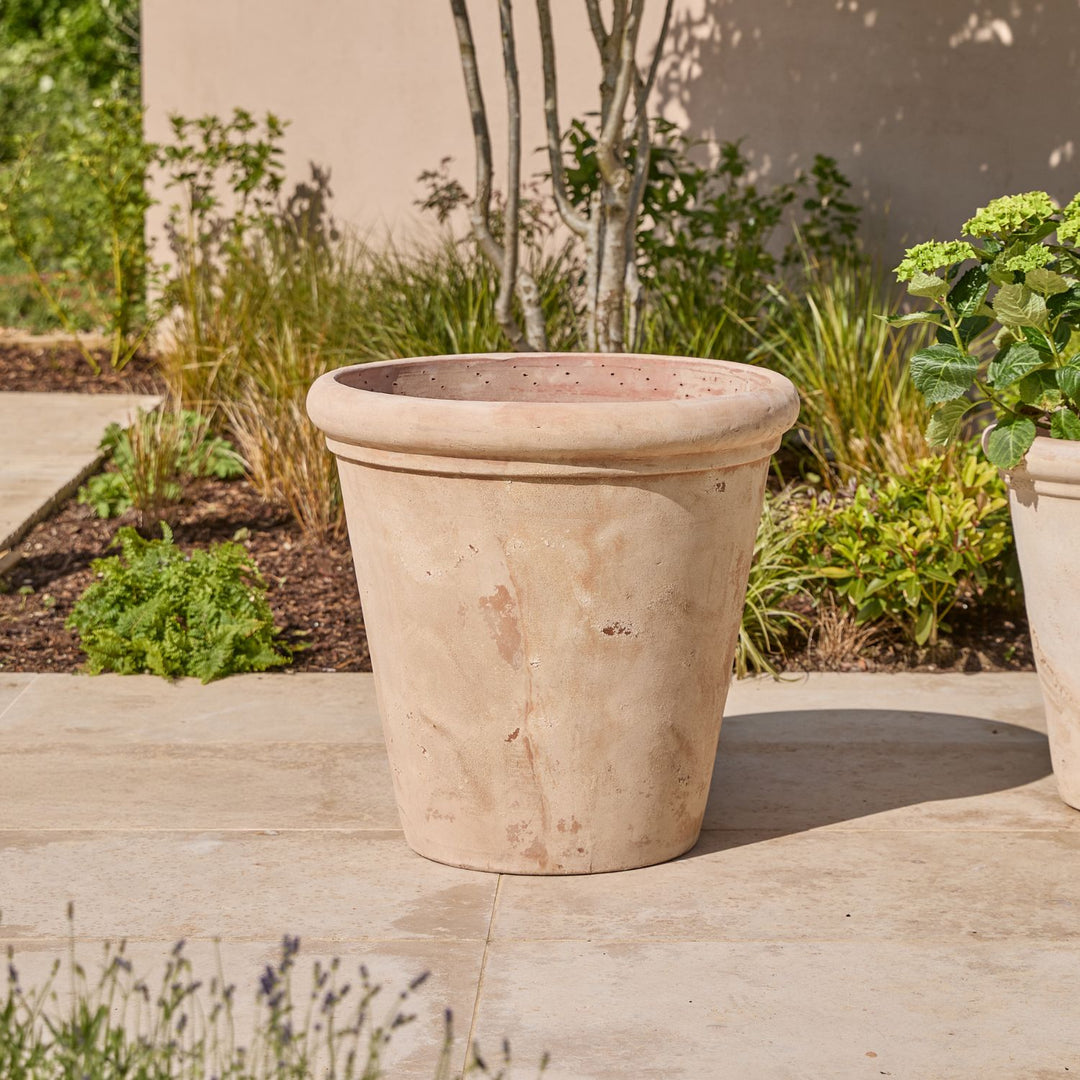 Beige antique terracotta pot on a patio with garden background