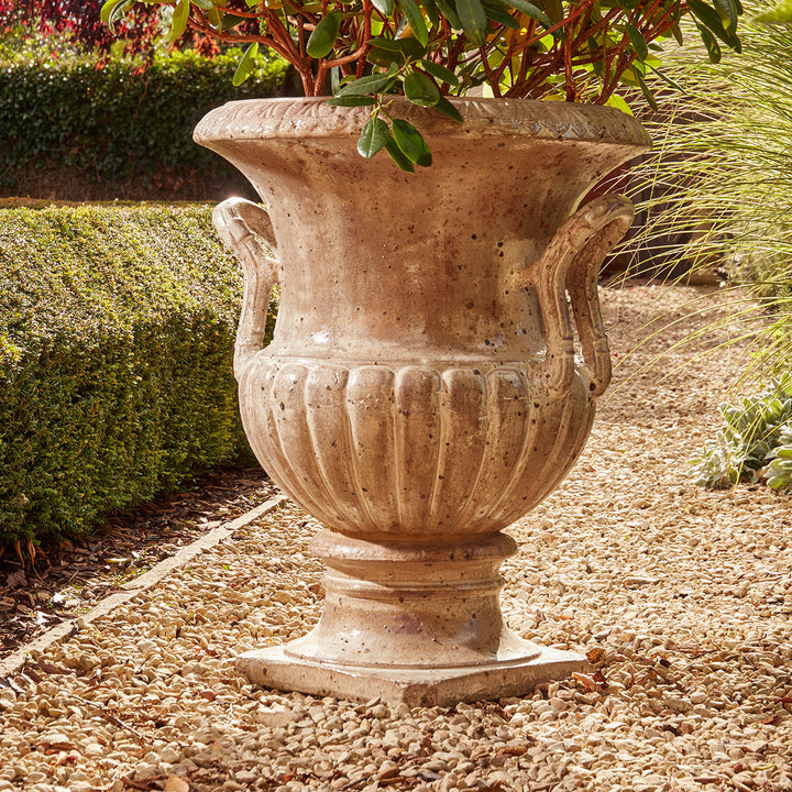 Large fluted garden urn with honey gloss glaze and classical handles, styled in a gravel path among structured hedging.