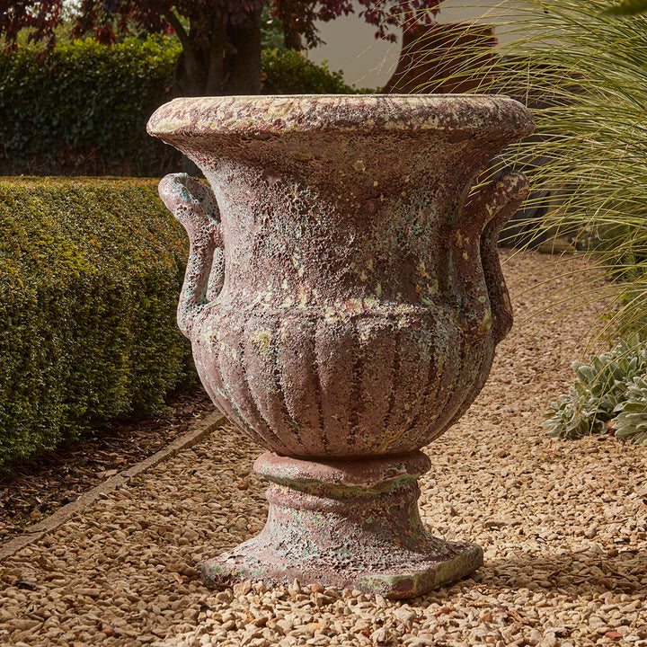 Large French-style urn planter with aged turquoise salt glaze finish and curved fluted body, placed on a traditional gravel garden path.