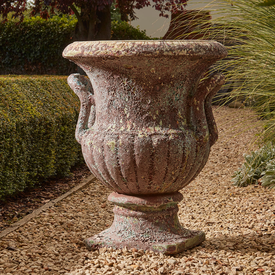 Large French-style urn planter with aged turquoise salt glaze finish and curved fluted body, placed on a traditional gravel garden path.