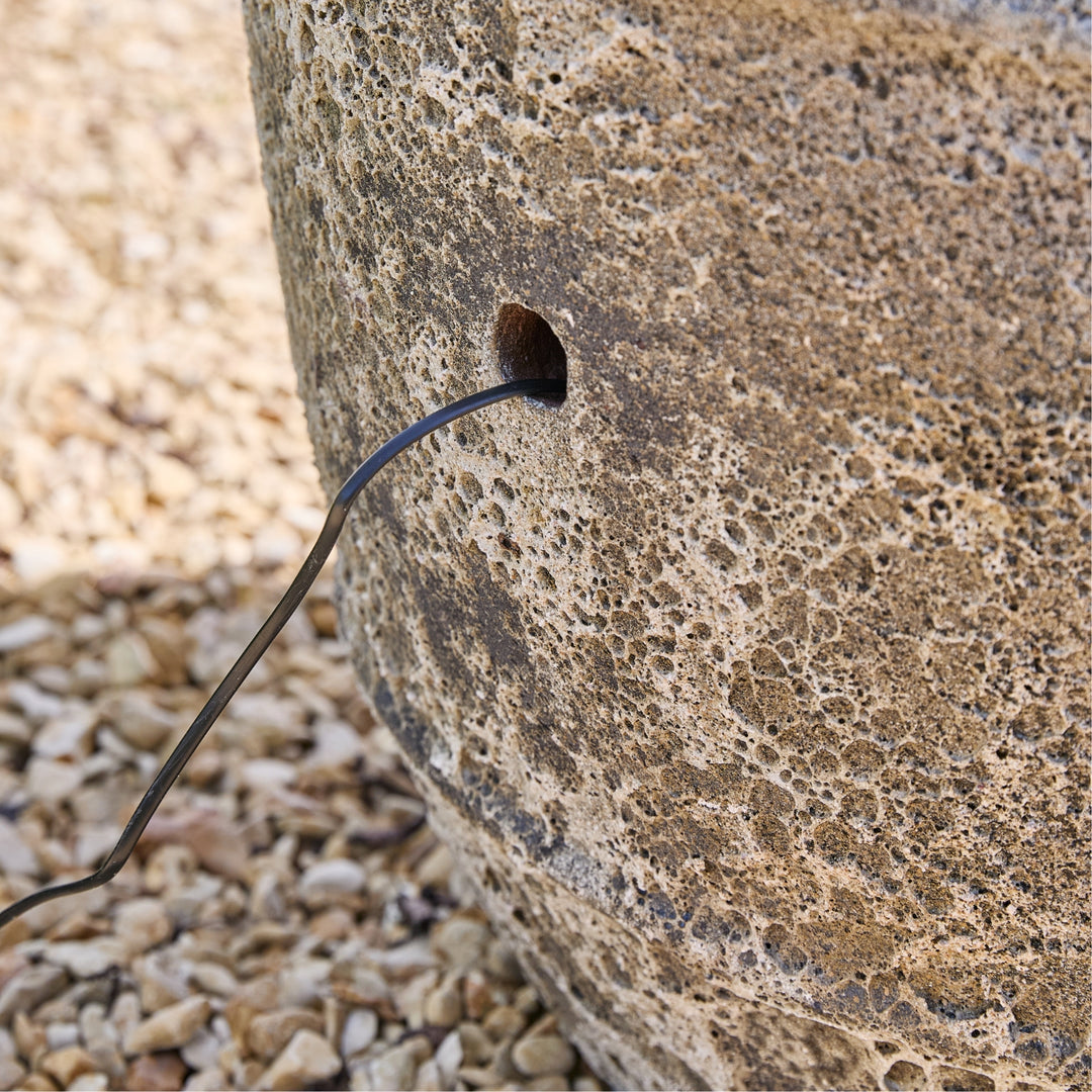 Black cable from a stone wall on a gravel surface