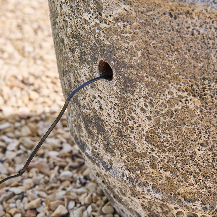 Black cable from a stone wall on a gravel surface