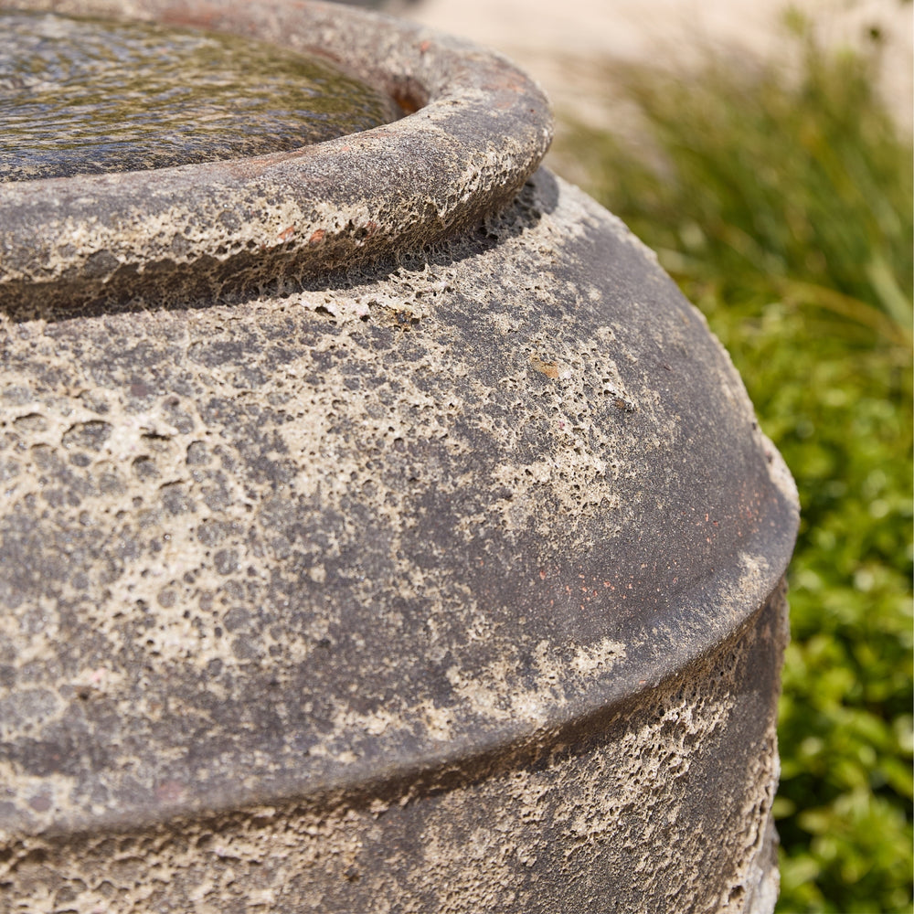 Close-up of a textured stone water feature with greenery in the background