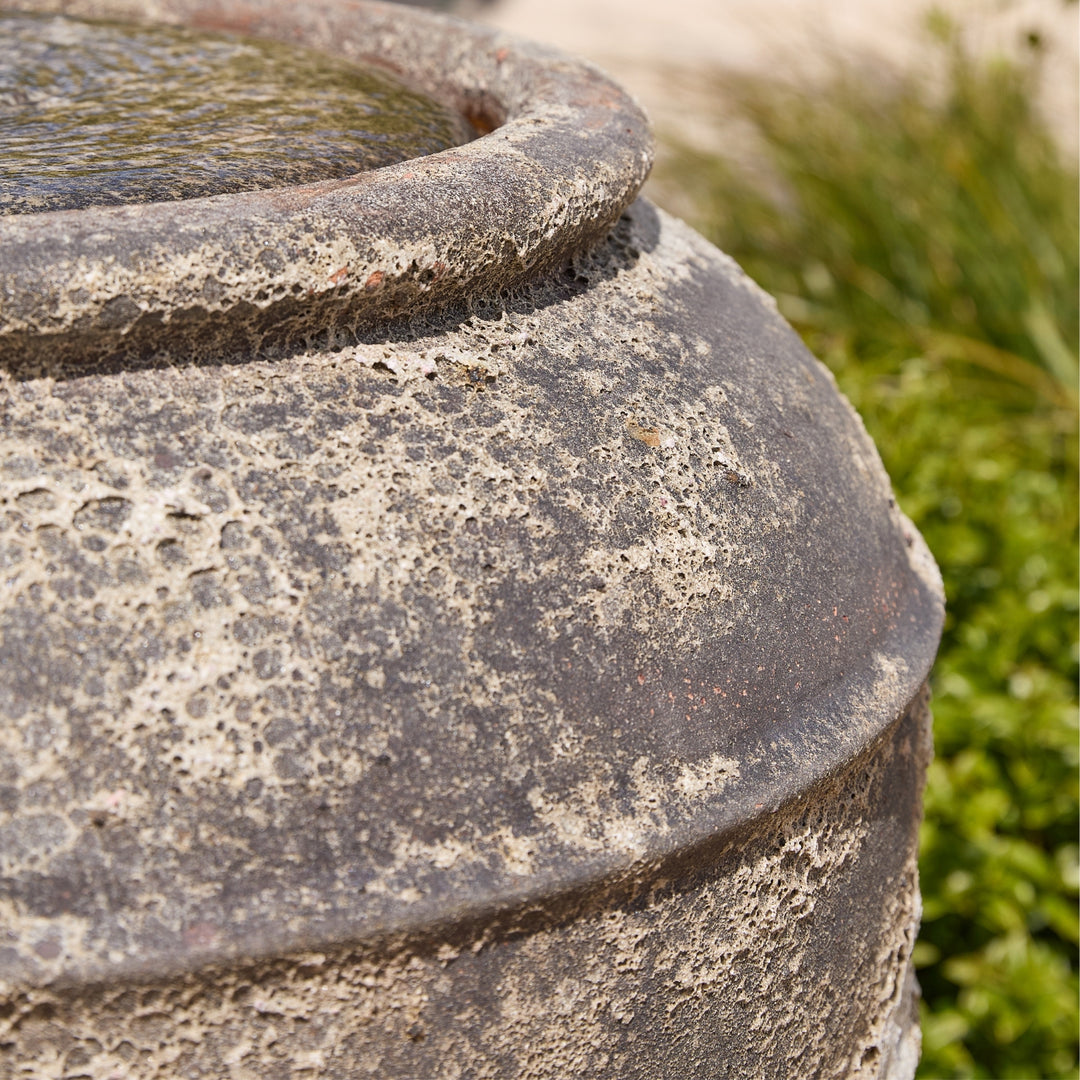Close-up of a textured stone water feature with greenery in the background