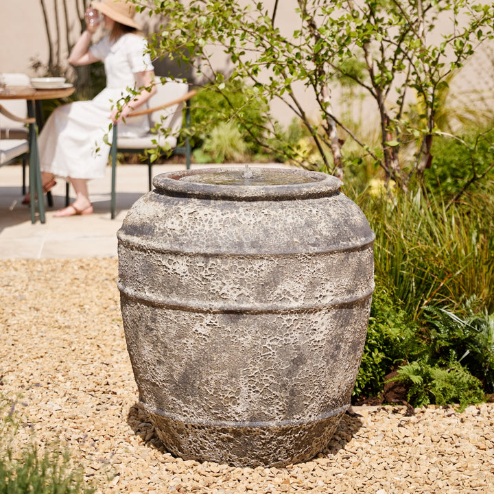Decorative stone water feature in a garden setting with a person sitting in the background.