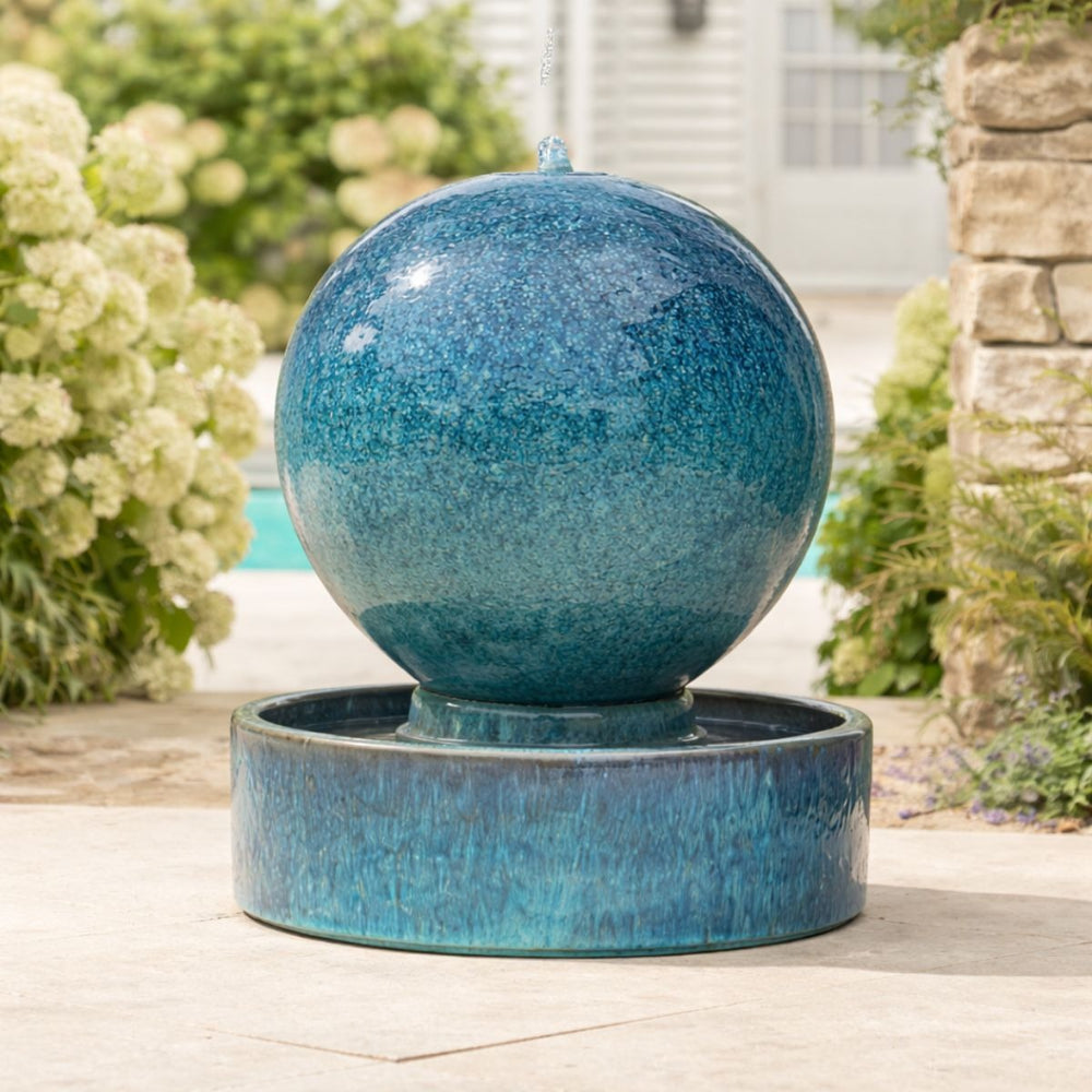 Extra-large globe-shaped ceramic water feature with a aqua blue glaze and integrated basin, styled on a garden patio.