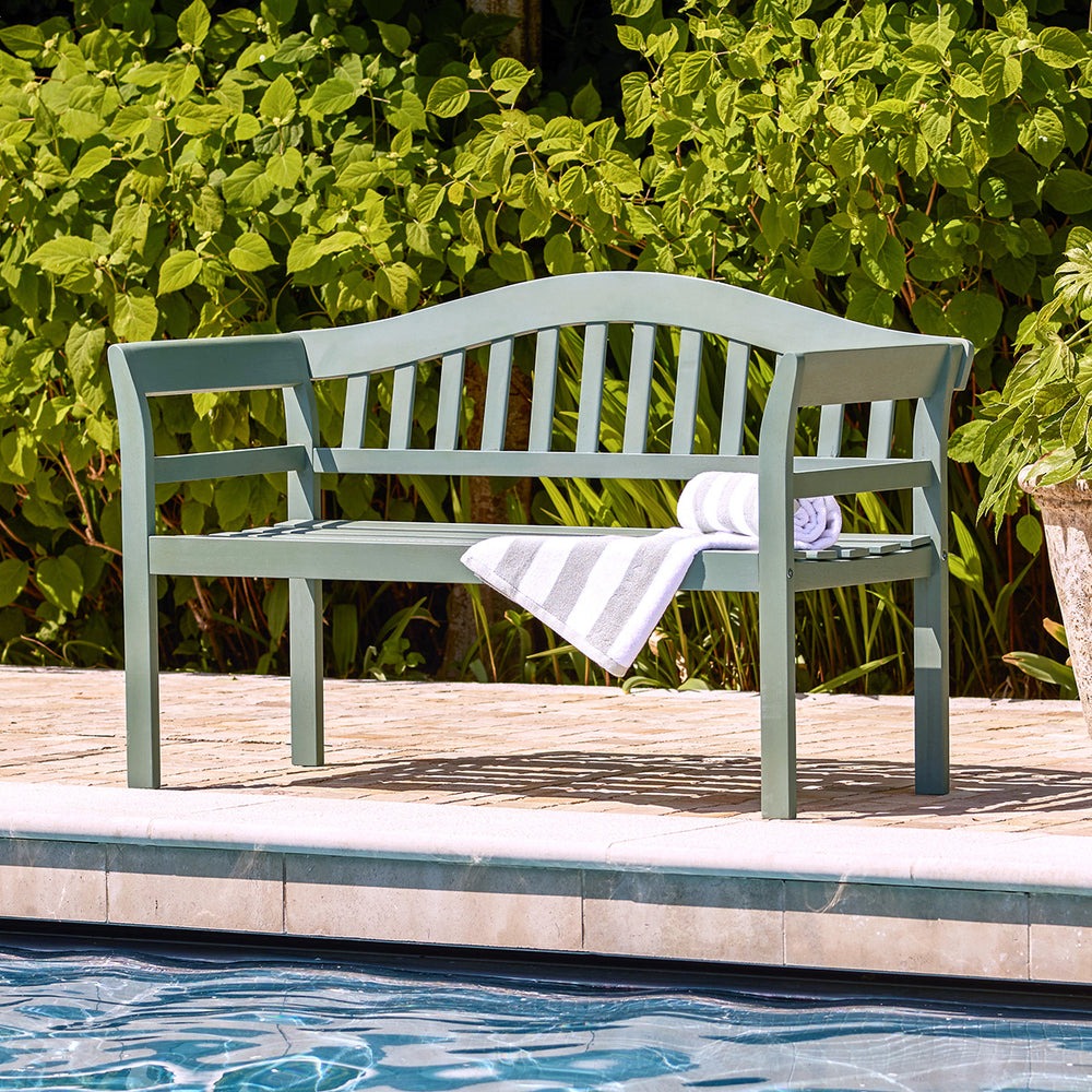 Green painted 2 seater bench styled with a striped towel by a poolside, perfect for relaxed outdoor living.