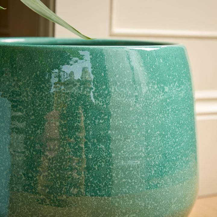 Green ceramic indoor plant pot with speckled texture on a white tiled wall background