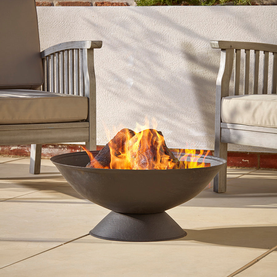 A black cast iron fire pit with a lit fire, placed on a cotswold courtyard garden, creating a cozy outdoor atmosphere.