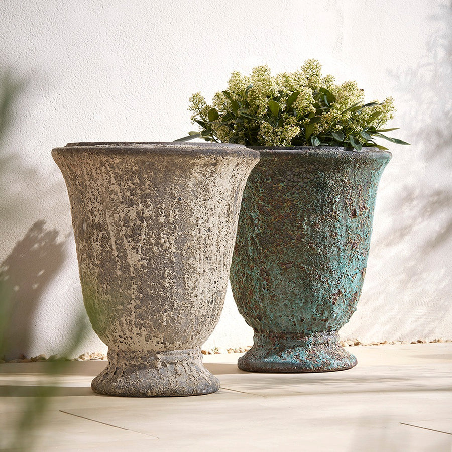 Two rustic-style stone planters with one containing greenery against a white wall.