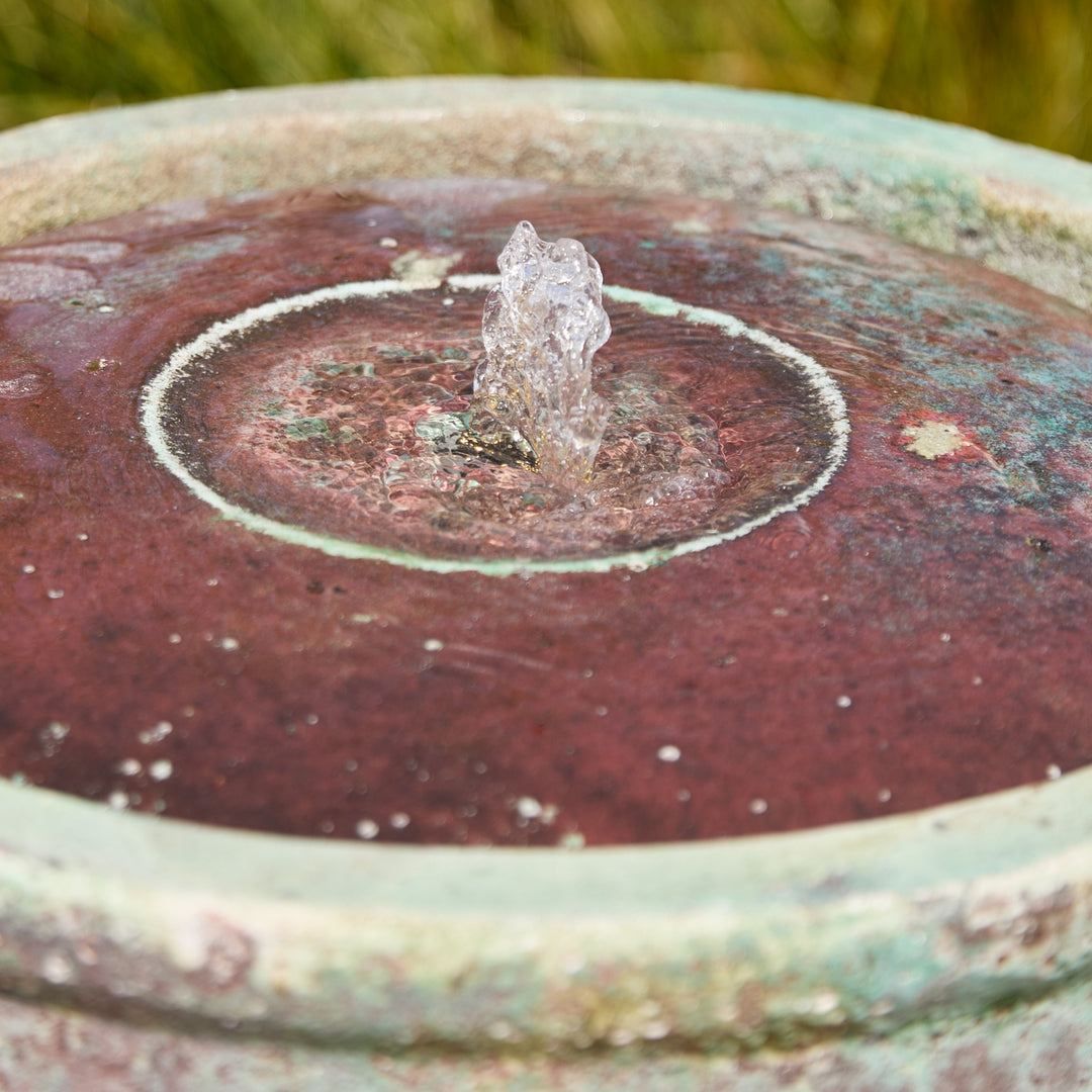 Close-up of a rustic stone water fountain with water spraying out.